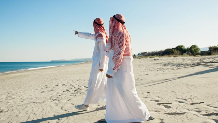 Two men in traditional dress walking along a Gulf beach