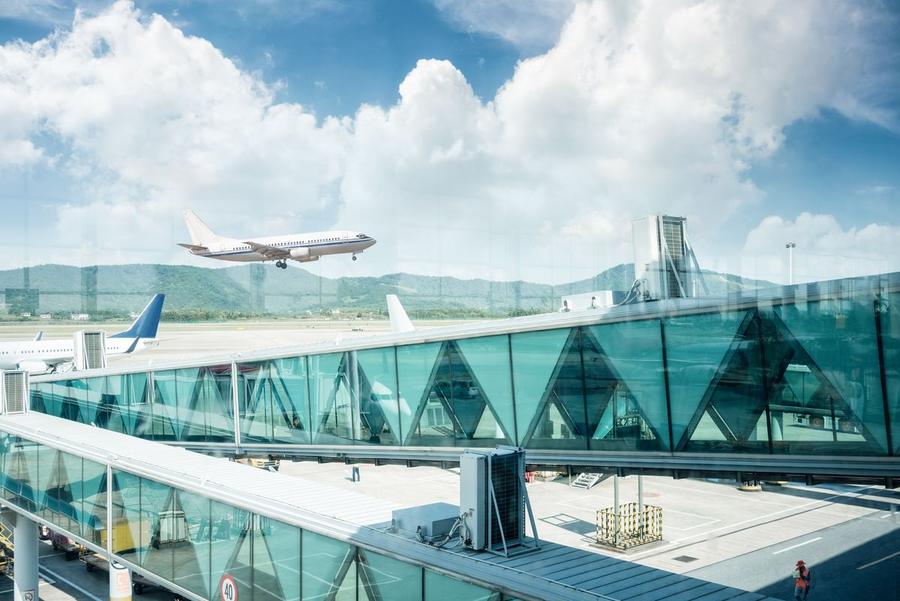 Aircraft taking off beyond a glass airport jet bridge