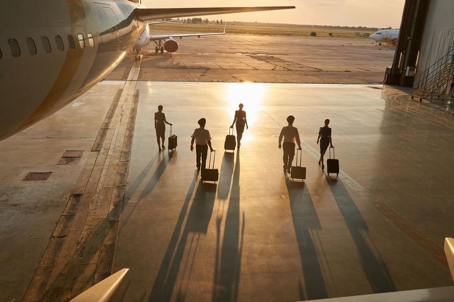 Travellers walking with luggage towards an aircraft at sunrise